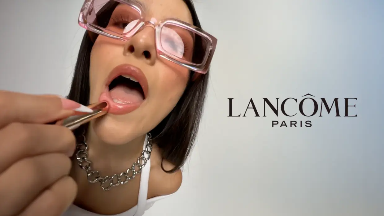 Lancôme Paris beauty product launch creative, model in pink glasses applying lip gloss