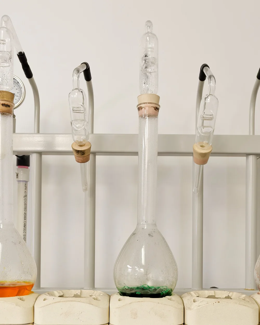 Volumetric flasks, one amber and one green, on a heating bench in the distillery lab. Photograph by Neville Palmer.